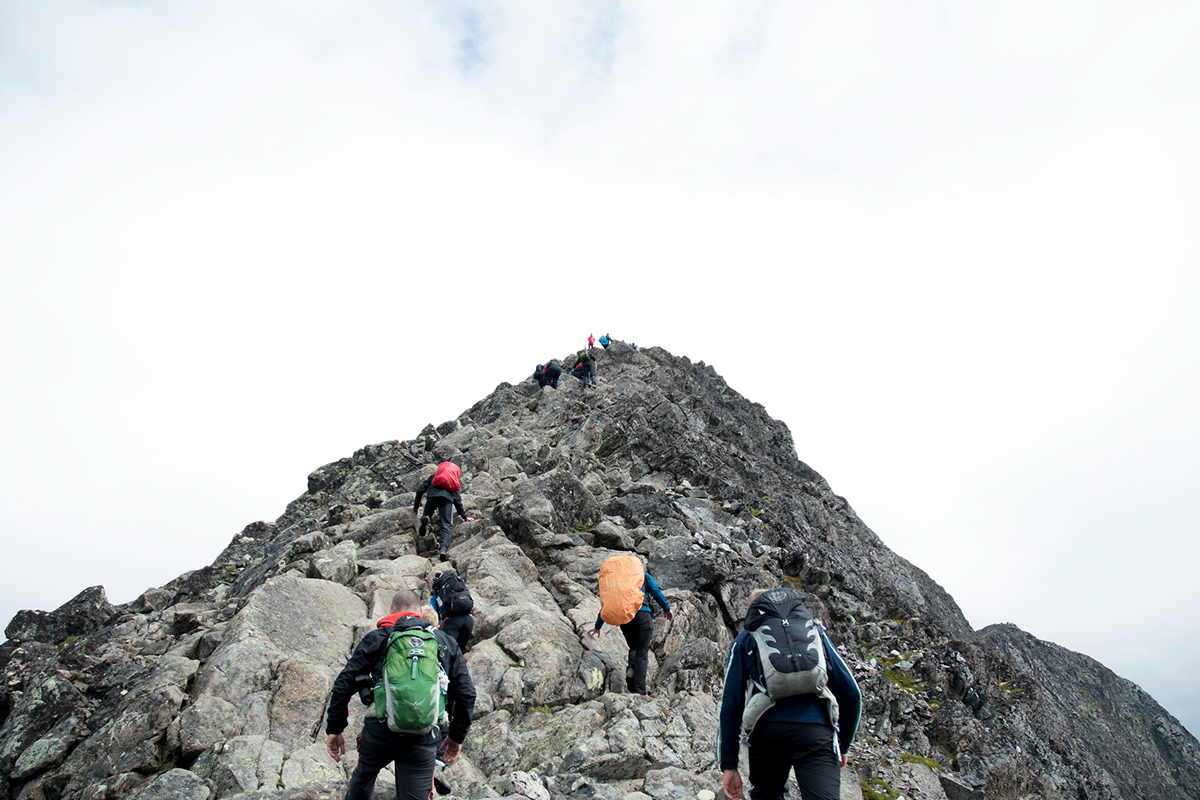 Zwei überlagerte Bilder zeigen eine Gruppe von Wanderern beim Aufstieg auf einen felsigen Berg und eine Gruppe auf dem Gipfel unter strahlend blauem Himmel mit weißen Wolken. Der eingeblendete Text lautet: „Finden Sie den Lernpfad, der Sie wirklich weiterbringt.“ – die Szene symbolisiert persönliche Weiterentwicklung, Zielstrebigkeit und das Erreichen neuer Höhen.